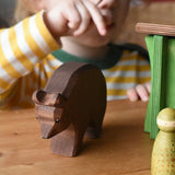 Ostheimer brown bear wooden toy figure placed on a wooden surface a child can be seen pointing in the background.
