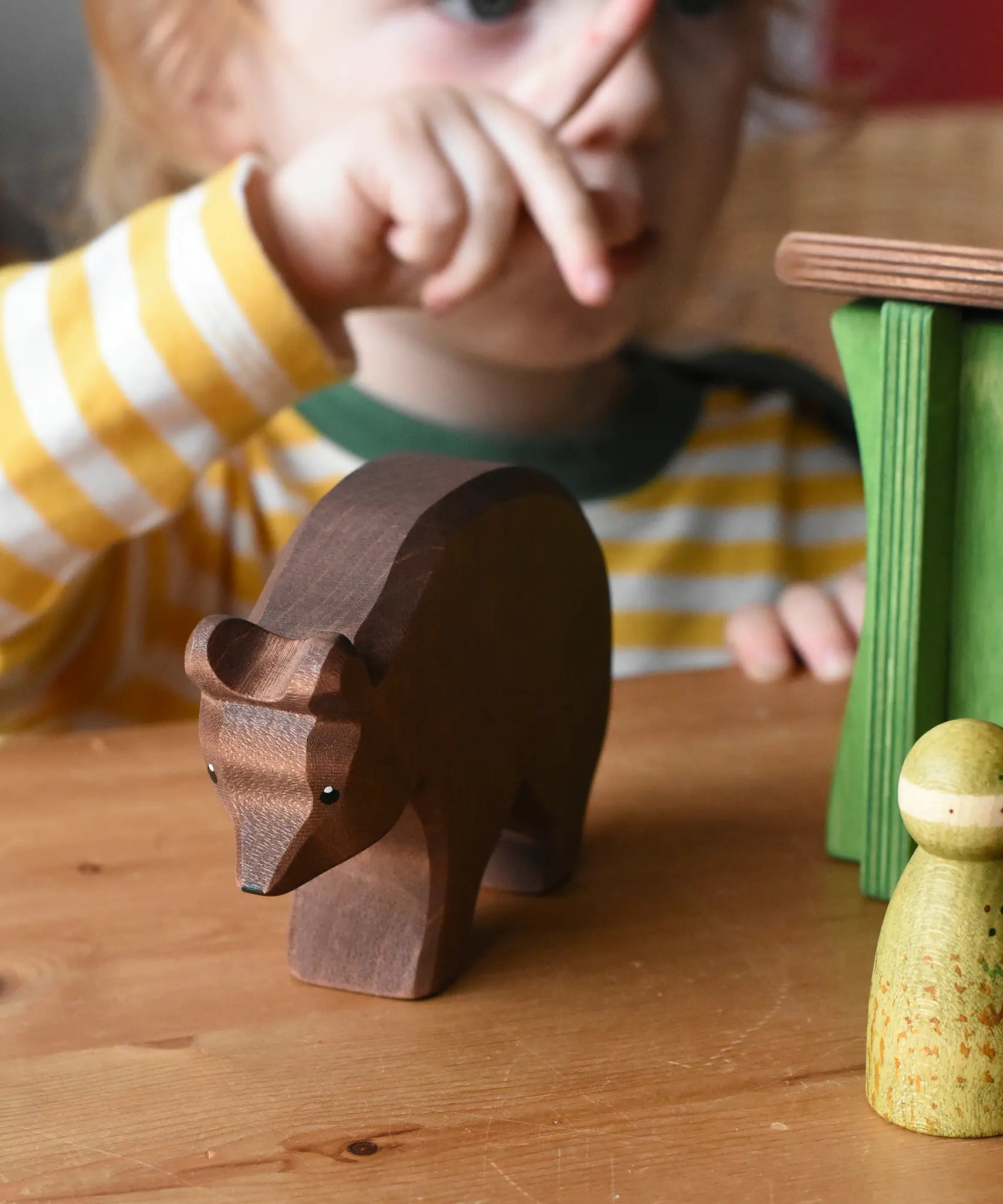 Ostheimer brown bear wooden toy figure placed on a wooden surface a child can be seen pointing in the background.