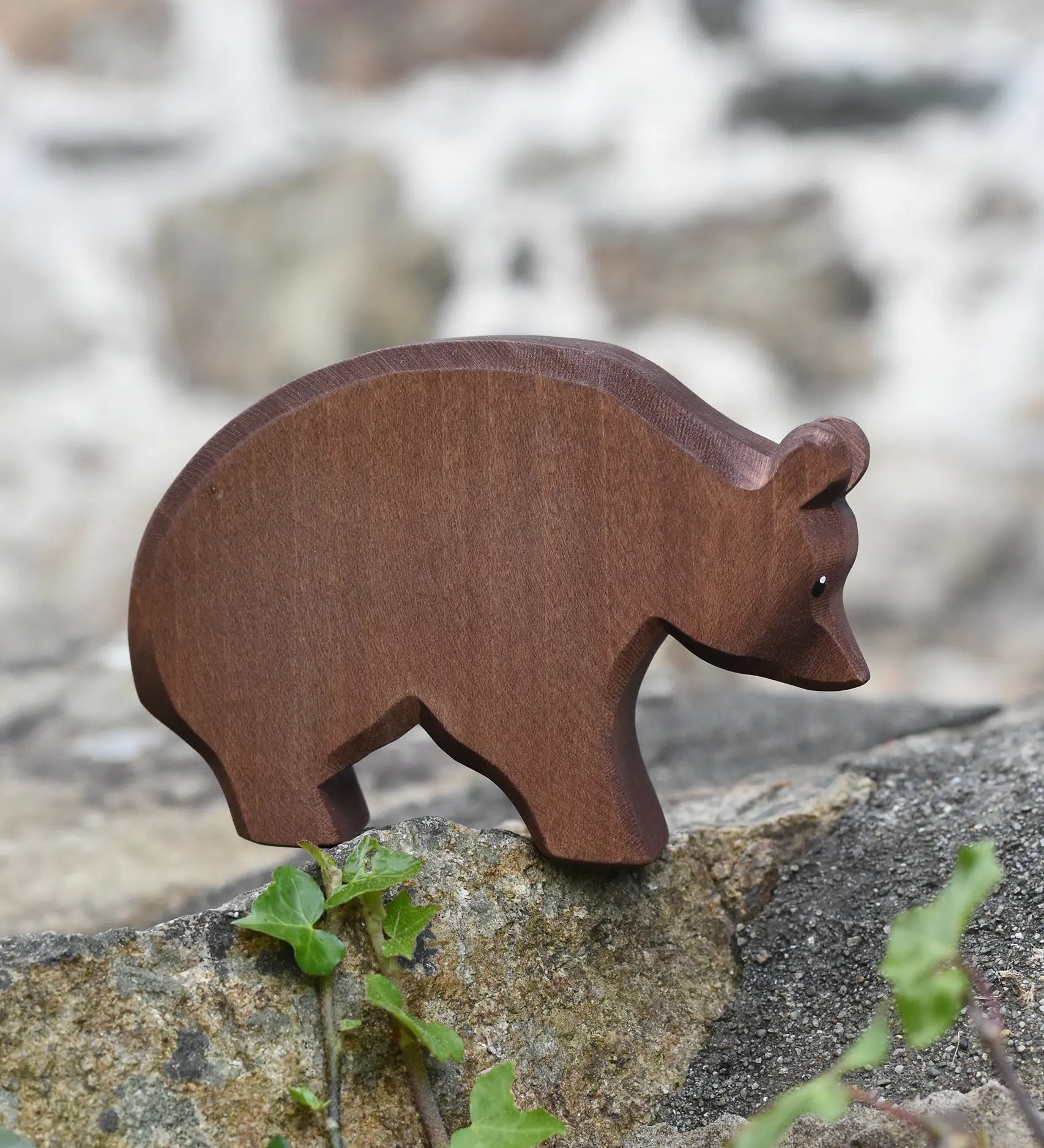 Ostheimer brown bear wooden toy figure placed on a stone wall outdoors.