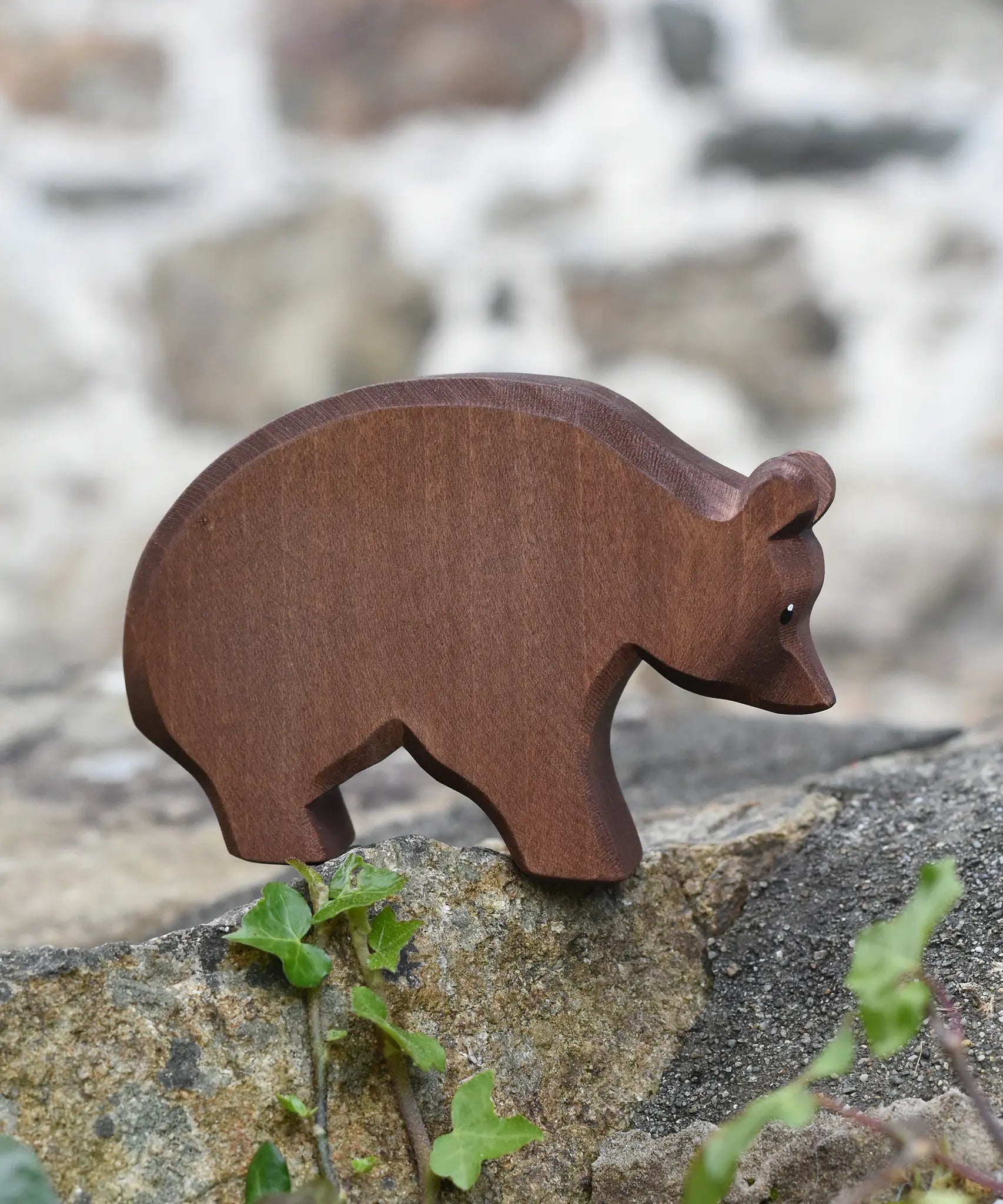 Ostheimer brown bear wooden toy figure placed on a stone wall outdoors.