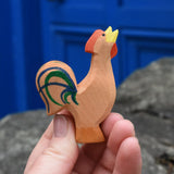 Ostheimer brown bremer rooster wooden toy figure in an adult's hand.