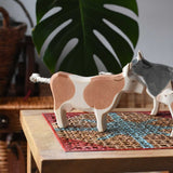 Ostheimer brown standing cow figure placed on a rattan stool in a simple small world play scene with other cows and calves in the background. 