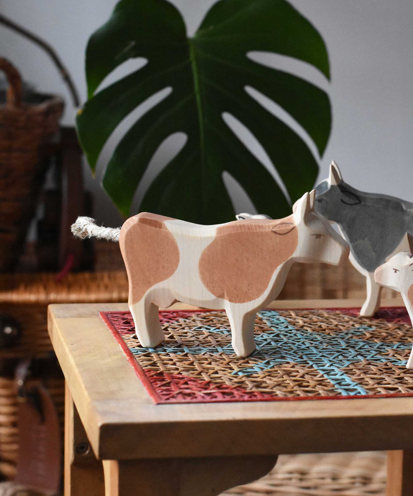 Ostheimer brown standing cow figure placed on a rattan stool in a simple small world play scene with other cows and calves in the background. 