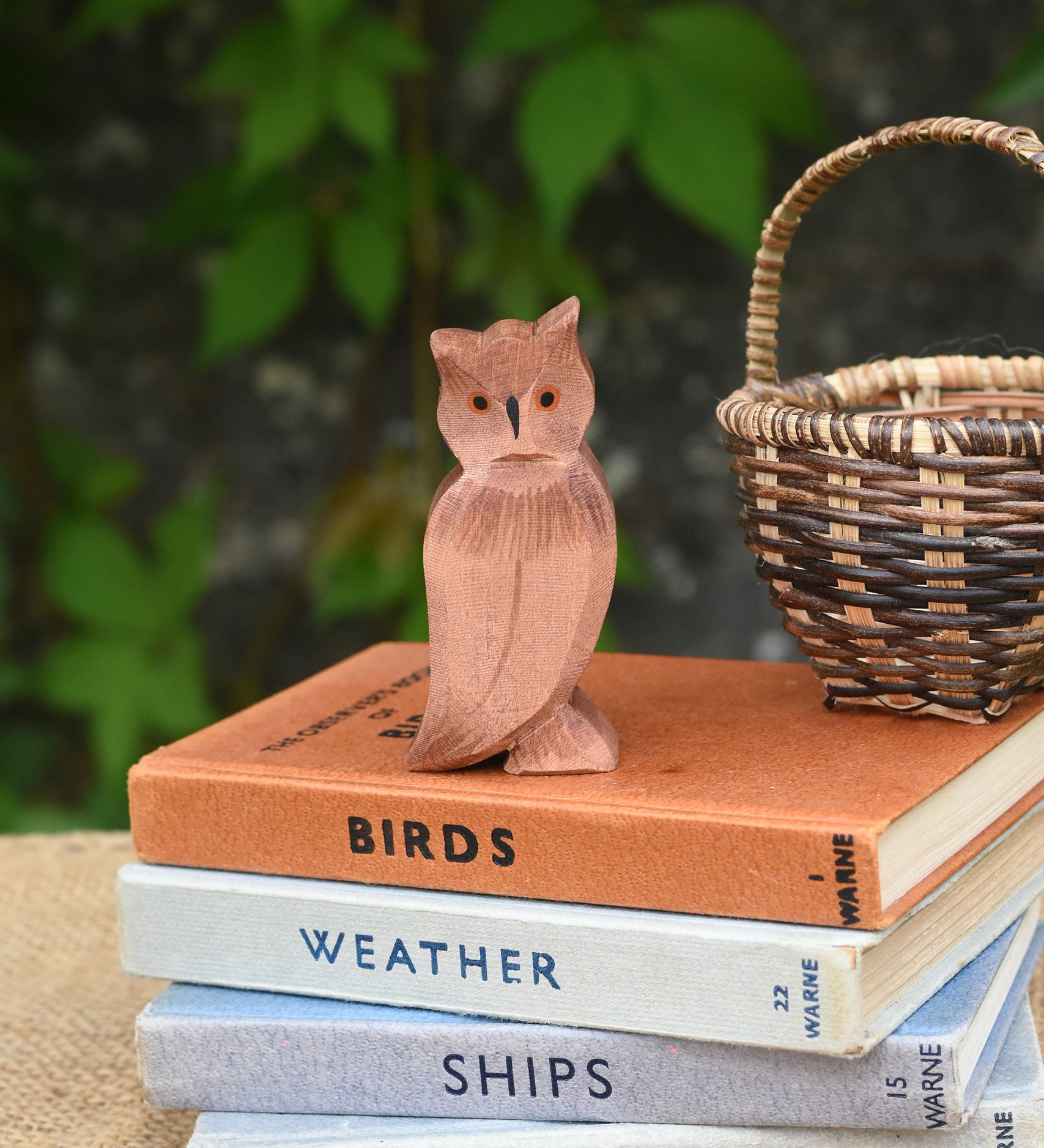 An Ostheimer brown coloured eagle owl placed on a pile of books next to a Kraul basket. The owl figure is part of a large collection of expertly hand crafted wooden toys and figures here at Babipur. 