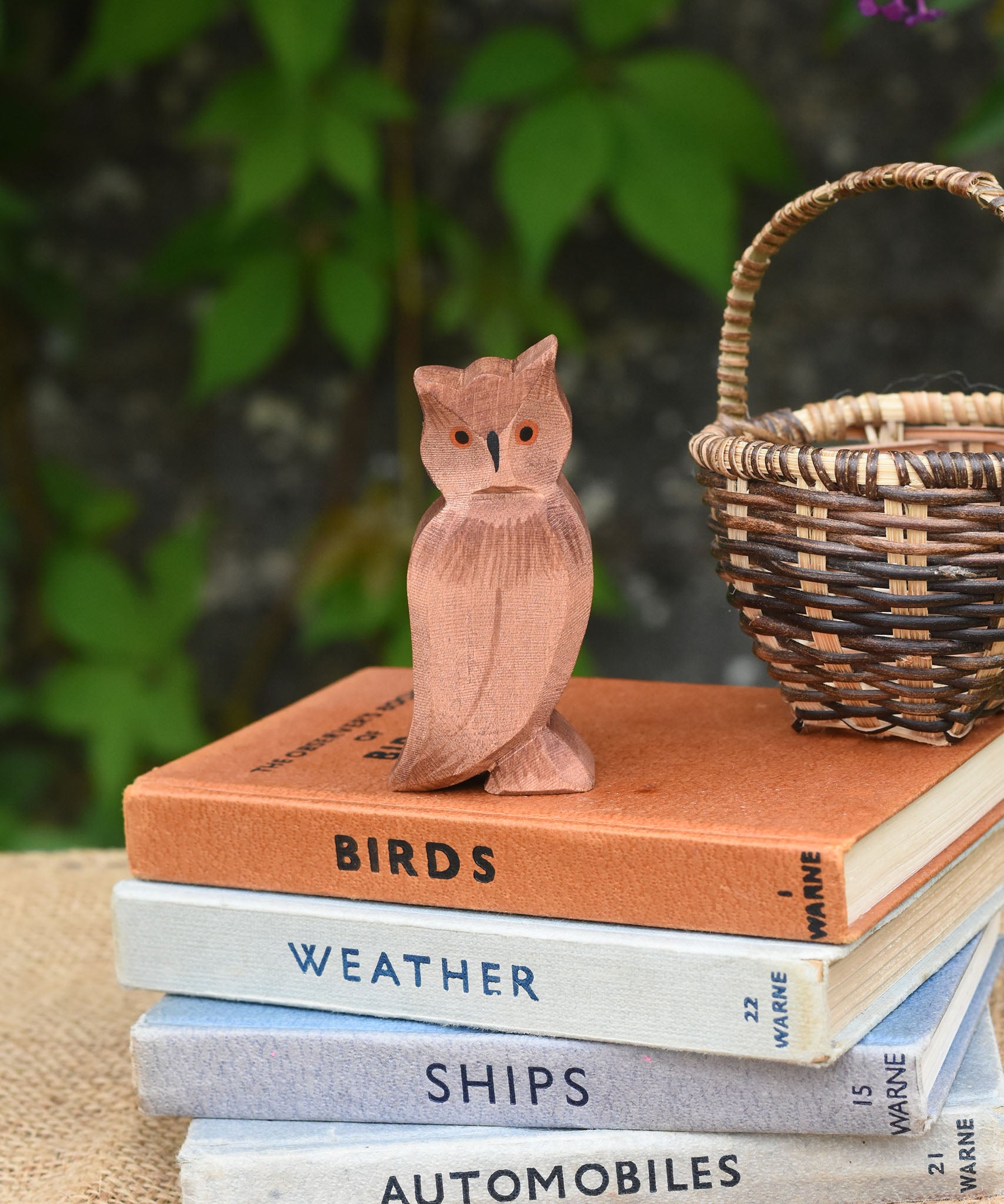 An Ostheimer brown coloured eagle owl placed on a pile of books next to a Kraul basket. The owl figure is part of a large collection of expertly hand crafted wooden toys and figures here at Babipur. 