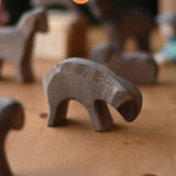 A Ostheimer Brown Eating Sheep wooden toy figure placed on a wooden surface. Other brown sheep figures can be seen in the background. This wooden figure is part of a large range of expertly hand crafted, Waldorf inspired, wooden toys here at Babipur. 