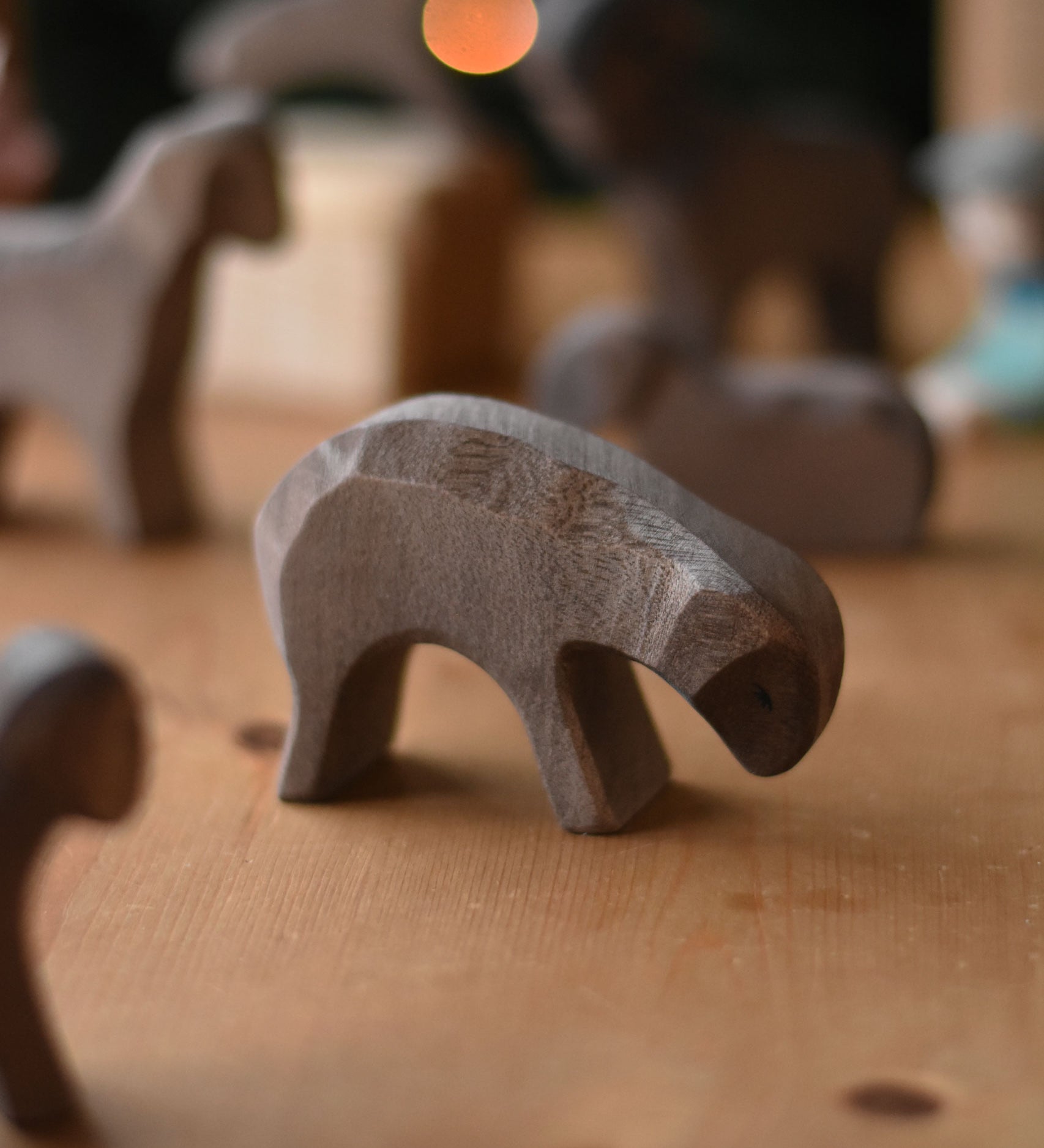 A Ostheimer Brown Eating Sheep wooden toy figure placed on a wooden surface. Other brown sheep figures can be seen in the background. This wooden figure is part of a large range of expertly hand crafted, Waldorf inspired, wooden toys here at Babipur. 
