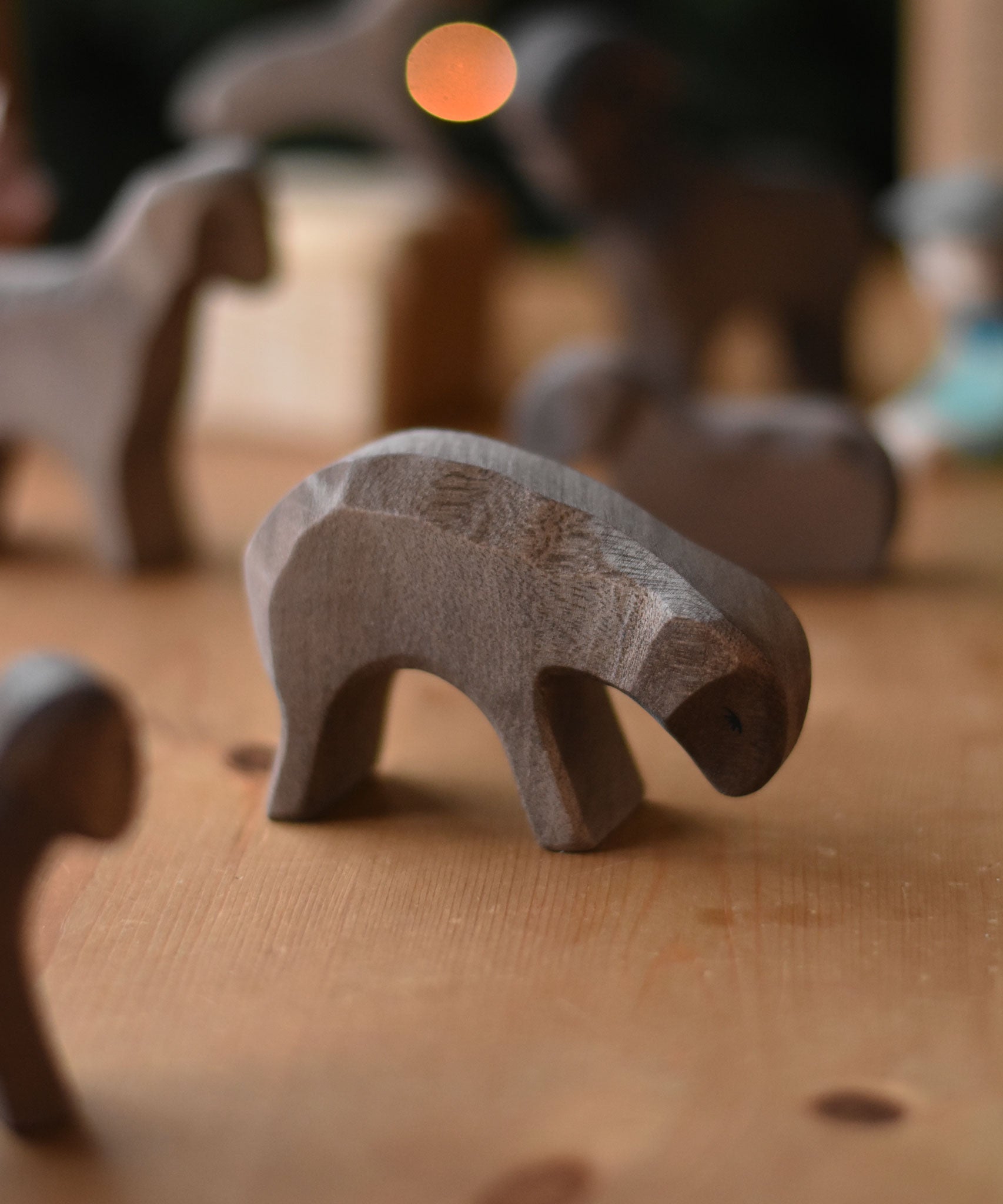 A Ostheimer Brown Eating Sheep wooden toy figure placed on a wooden surface. Other brown sheep figures can be seen in the background. This wooden figure is part of a large range of expertly hand crafted, Waldorf inspired, wooden toys here at Babipur. 