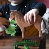 Close up of a child holding the Ostheimer brown horse wooden toy figure in a small world play scene. 