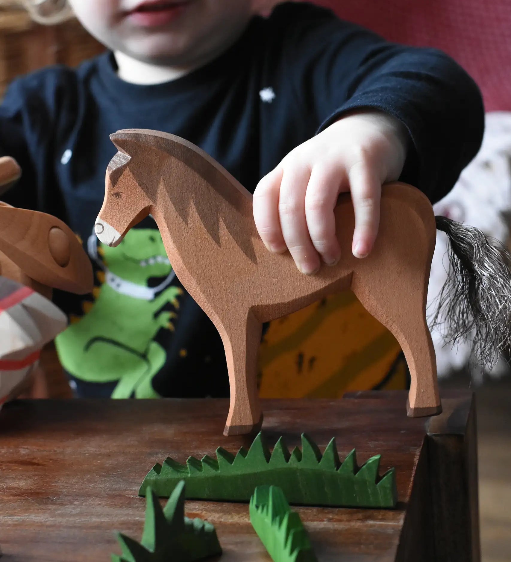 Close up of a child holding the Ostheimer brown horse wooden toy figure in a small world play scene. 