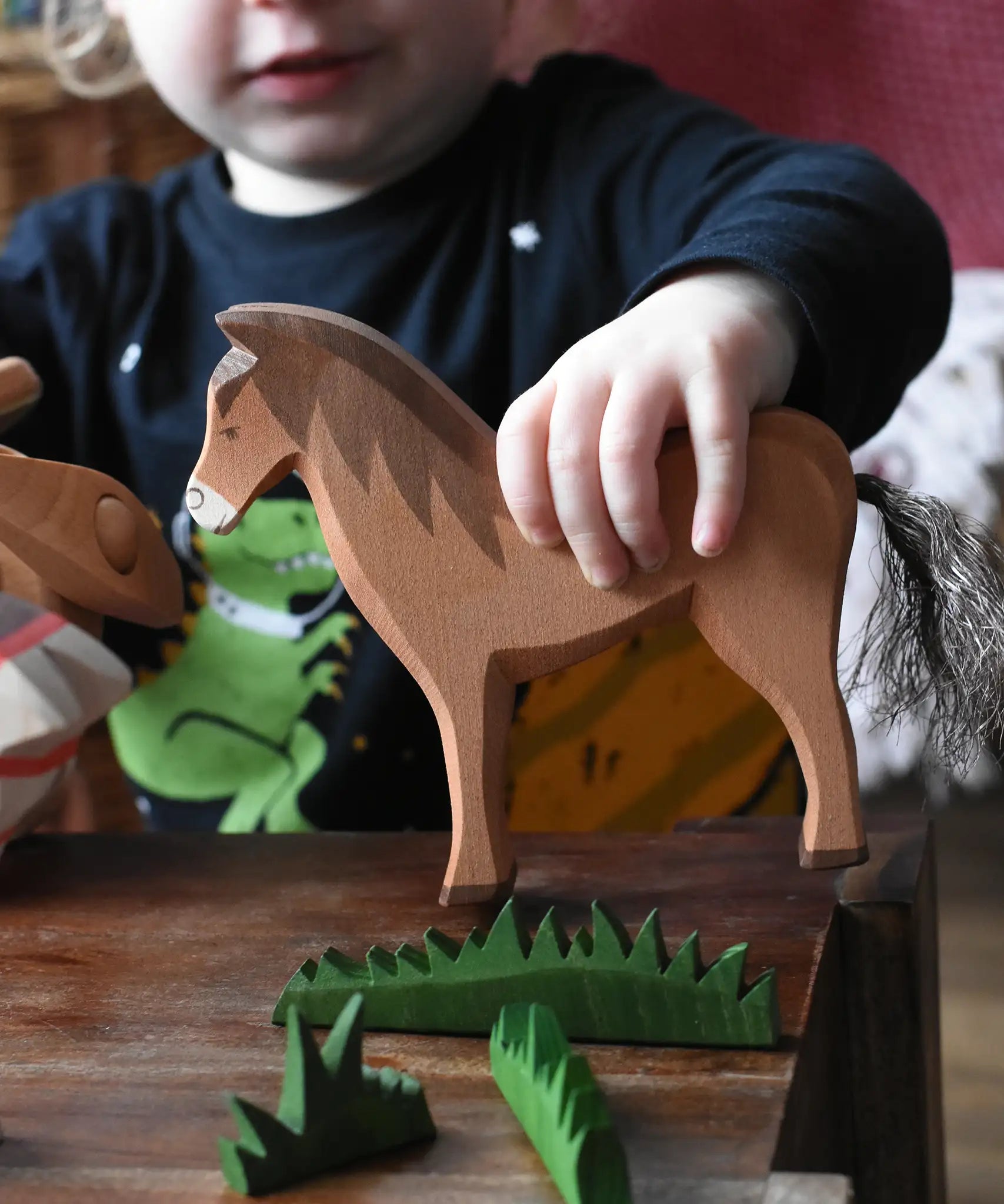 Close up of a child holding the Ostheimer brown horse wooden toy figure in a small world play scene. 