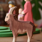 Ostheimer brown male goat wooden toy figure in front of stacked meadow plates. 