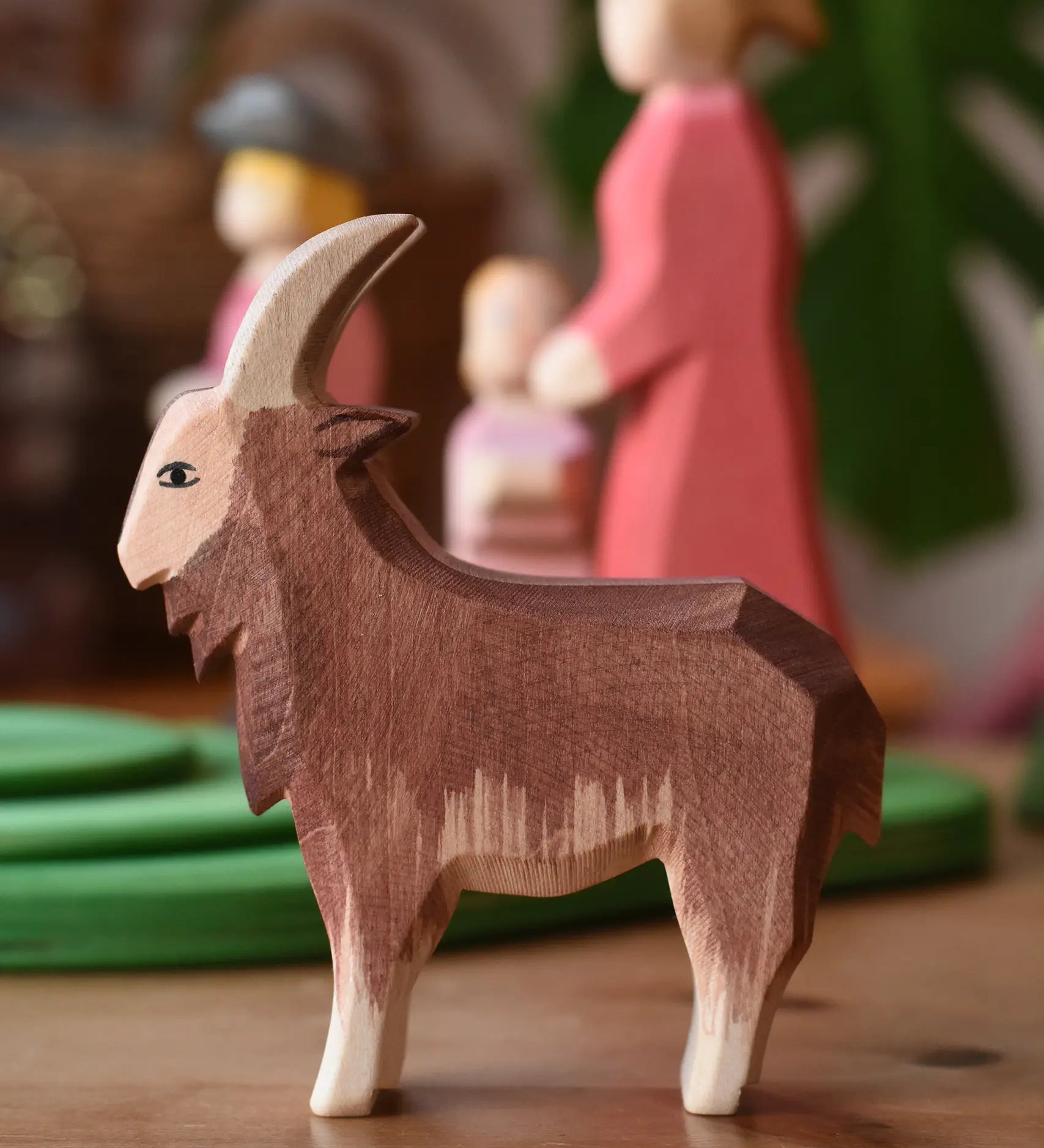 Ostheimer brown male goat wooden toy figure in front of stacked meadow plates. 