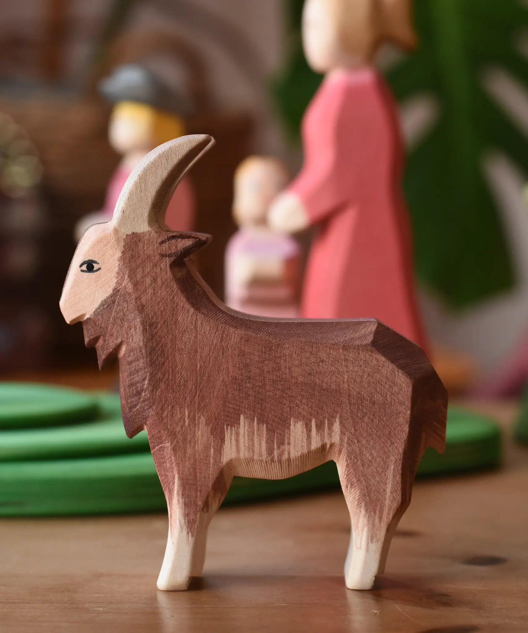 Ostheimer brown male goat wooden toy figure in front of stacked meadow plates. 