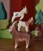 Three wooden toy goat figures stacked up on top of each other the Ostheimer brown male goat is at the bottom. 
