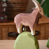 Ostheimer brown male goat wooden toy figure on a green bush piece. 