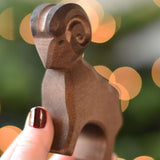 An Ostheimer Brown ram wooden toy figure in an adult's hand. This wooden figure is part of a large range of expertly hand crafted, Waldorf inspired, wooden toys here at Babipur. 