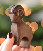 An Ostheimer Brown ram wooden toy figure in an adult's hand. This wooden figure is part of a large range of expertly hand crafted, Waldorf inspired, wooden toys here at Babipur. 