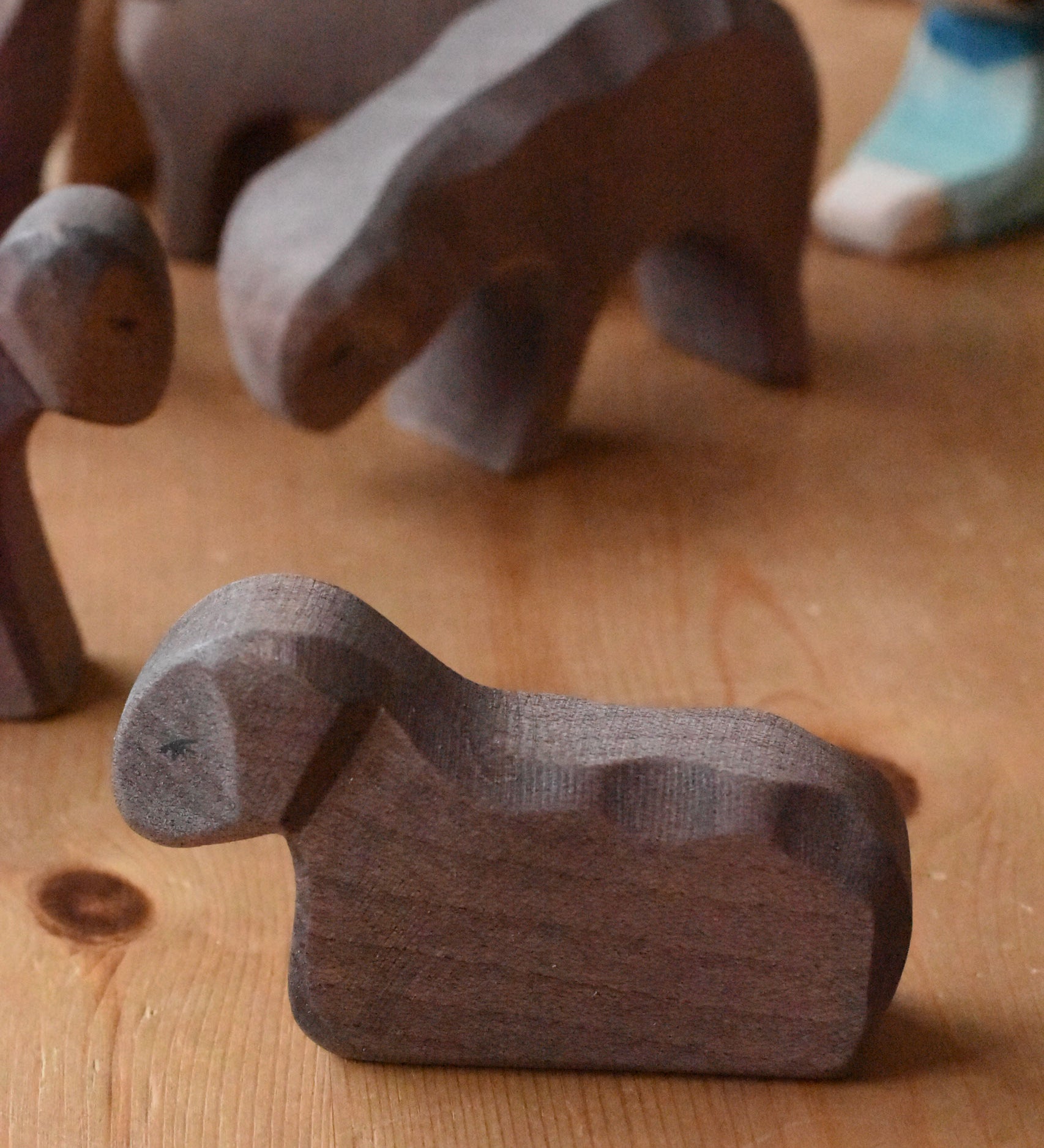 An Ostheimer Brown resting lamb wooden toy figure placed on a wooden surface. This wooden figure is part of a large range of expertly hand crafted, Waldorf inspired, wooden toys here at Babipur. 