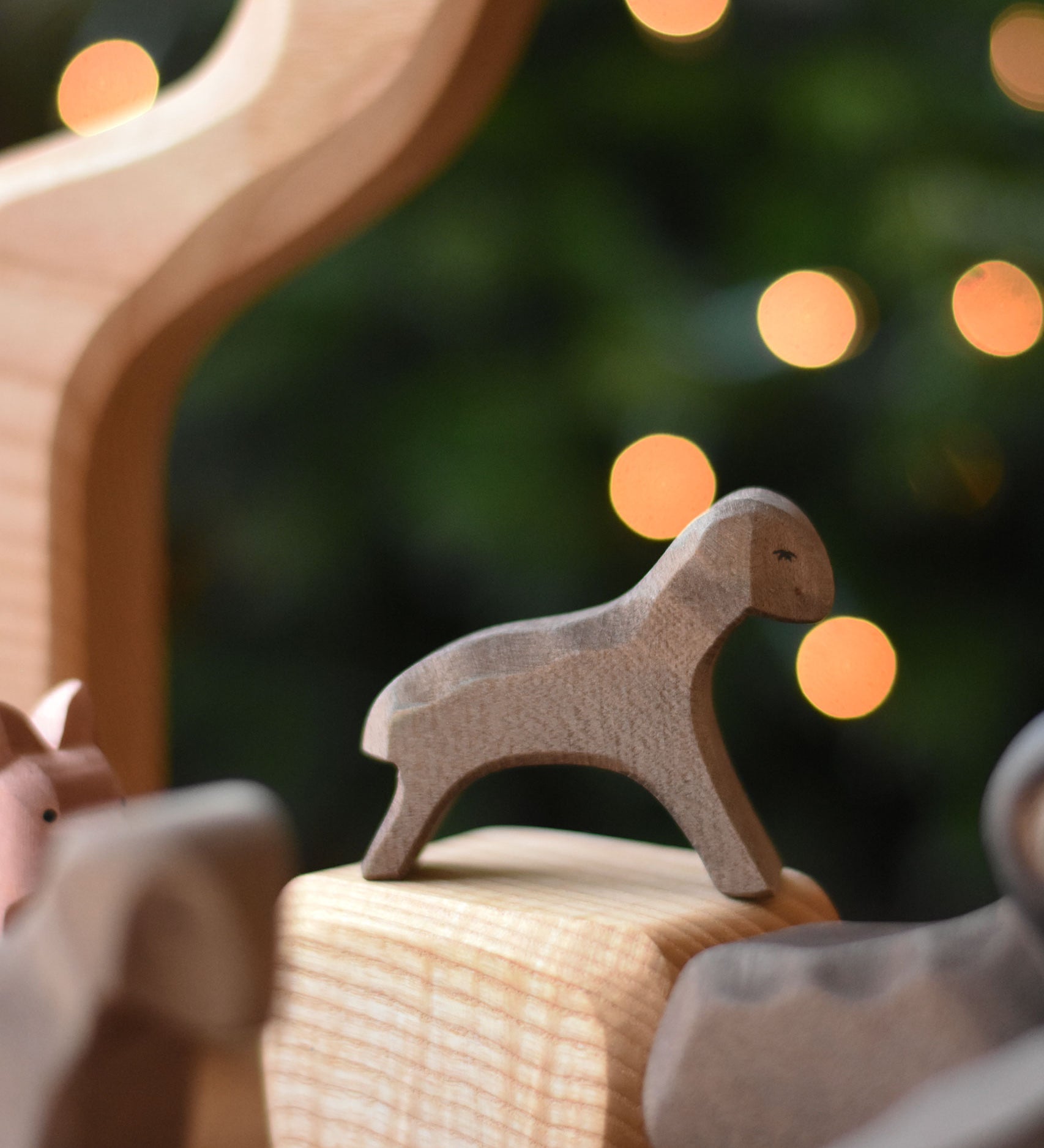 An Ostheimer Brown running lamb wooden toy figure placed on a wooden  block included in the Ostheimer 4 piece house set. This wooden figure is part of a large range of expertly hand crafted, Waldorf inspired, wooden toys here at Babipur. 