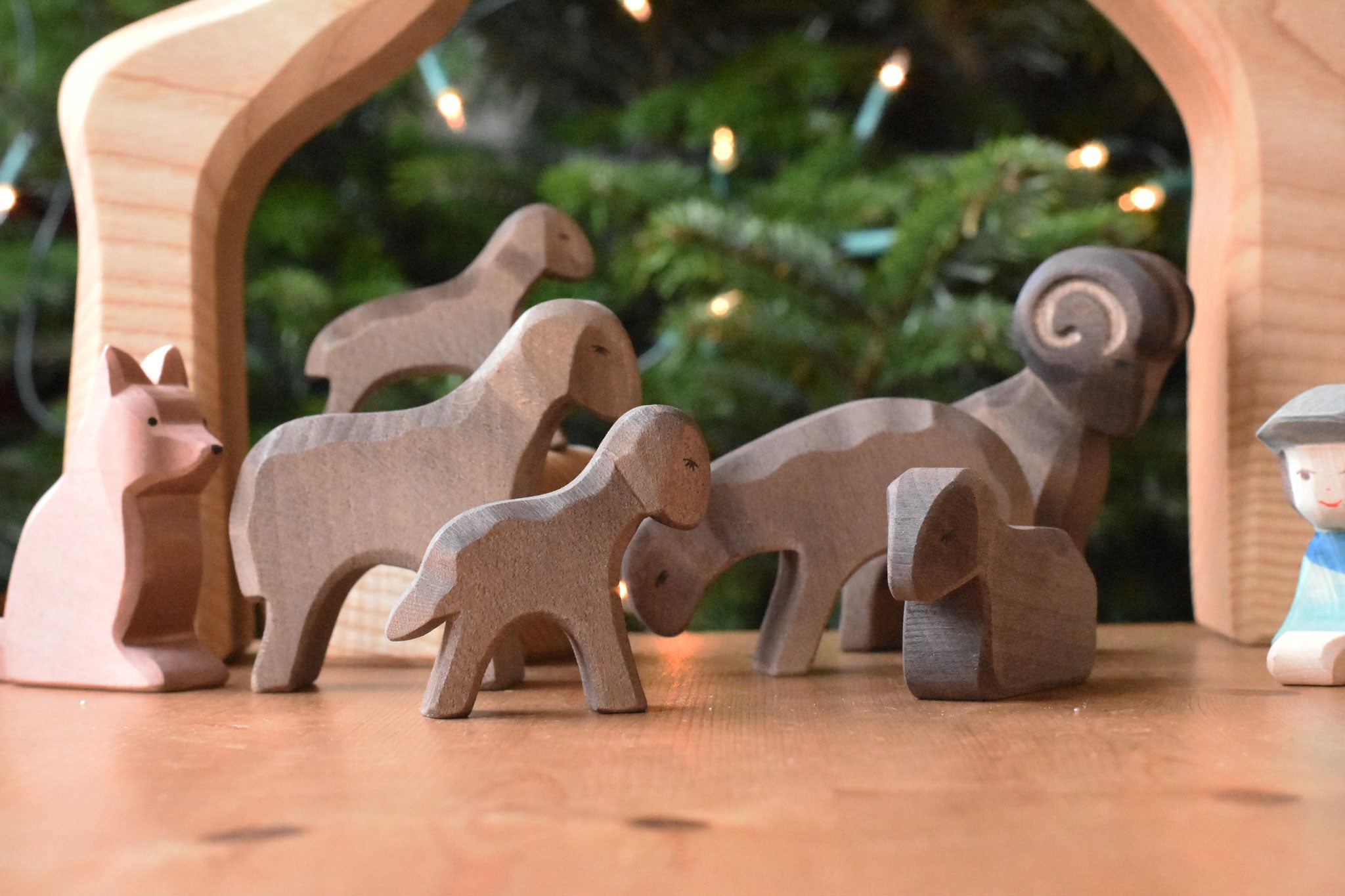 A collection of Ostheimer Brown Sheep wooden toy figures placed on a wooden surface along with a shepherd and shepherd's dog. These wooden figure is part of a large range of expertly hand crafted, Waldorf inspired, wooden toys here at Babipur. 