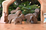 A collection of Ostheimer Brown Sheep wooden toy figures placed on a wooden surface along with a shepherd and shepherd's dog. These wooden figure is part of a large range of expertly hand crafted, Waldorf inspired, wooden toys here at Babipur. 