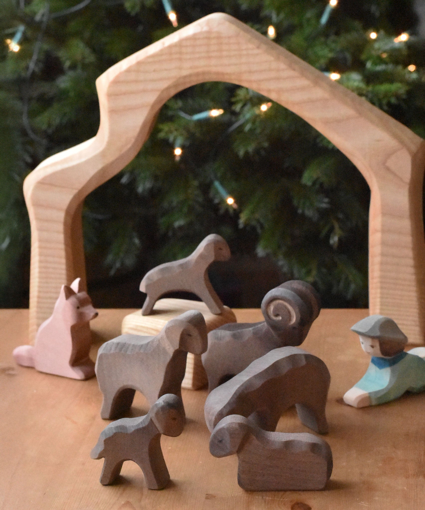 A collection of Ostheimer Brown Sheep wooden toy figures placed on a wooden surface along with a shepherd and shepherd's dog. These wooden figure is part of a large range of expertly hand crafted, Waldorf inspired, wooden toys here at Babipur. 