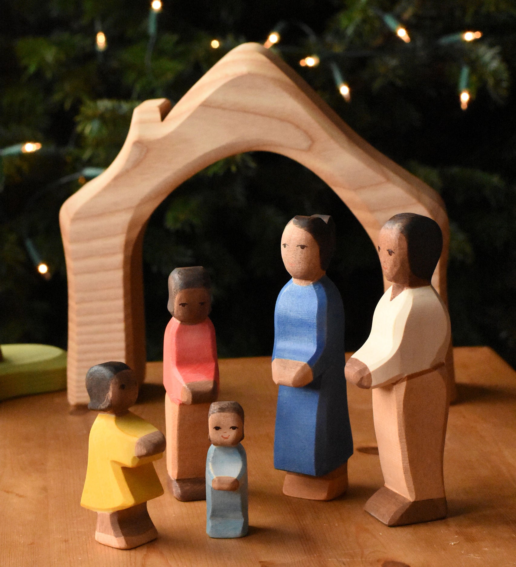 A family of Ostheimer figures with brown skin. There is a mother, father, son, daughter and toddler figure. The figures are all placed gathered together in front of the wooden house shaped piece from the Ostheimer 4 piece house set. These wooden figures are part of a wide range of expertly hand crafted wooden toys here at Babipur.