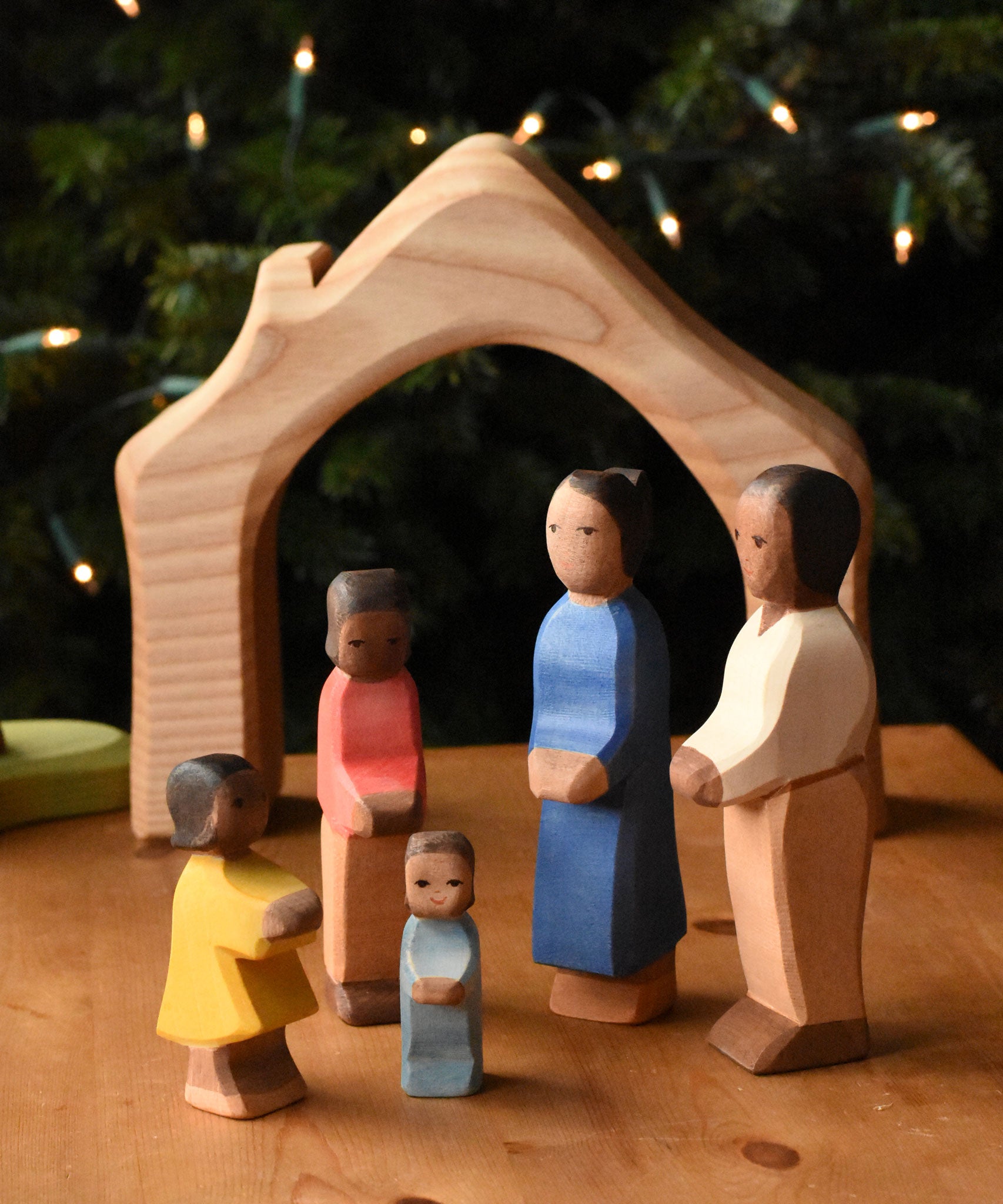 A family of Ostheimer figures with brown skin. There is a mother, father, son, daughter and toddler figure. The figures are all placed gathered together in front of the wooden house shaped piece from the Ostheimer 4 piece house set. These wooden figures are part of a wide range of expertly hand crafted wooden toys here at Babipur.