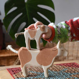 Child stacking a standing brown calf wooden toy figure on top of a brown cow figure.