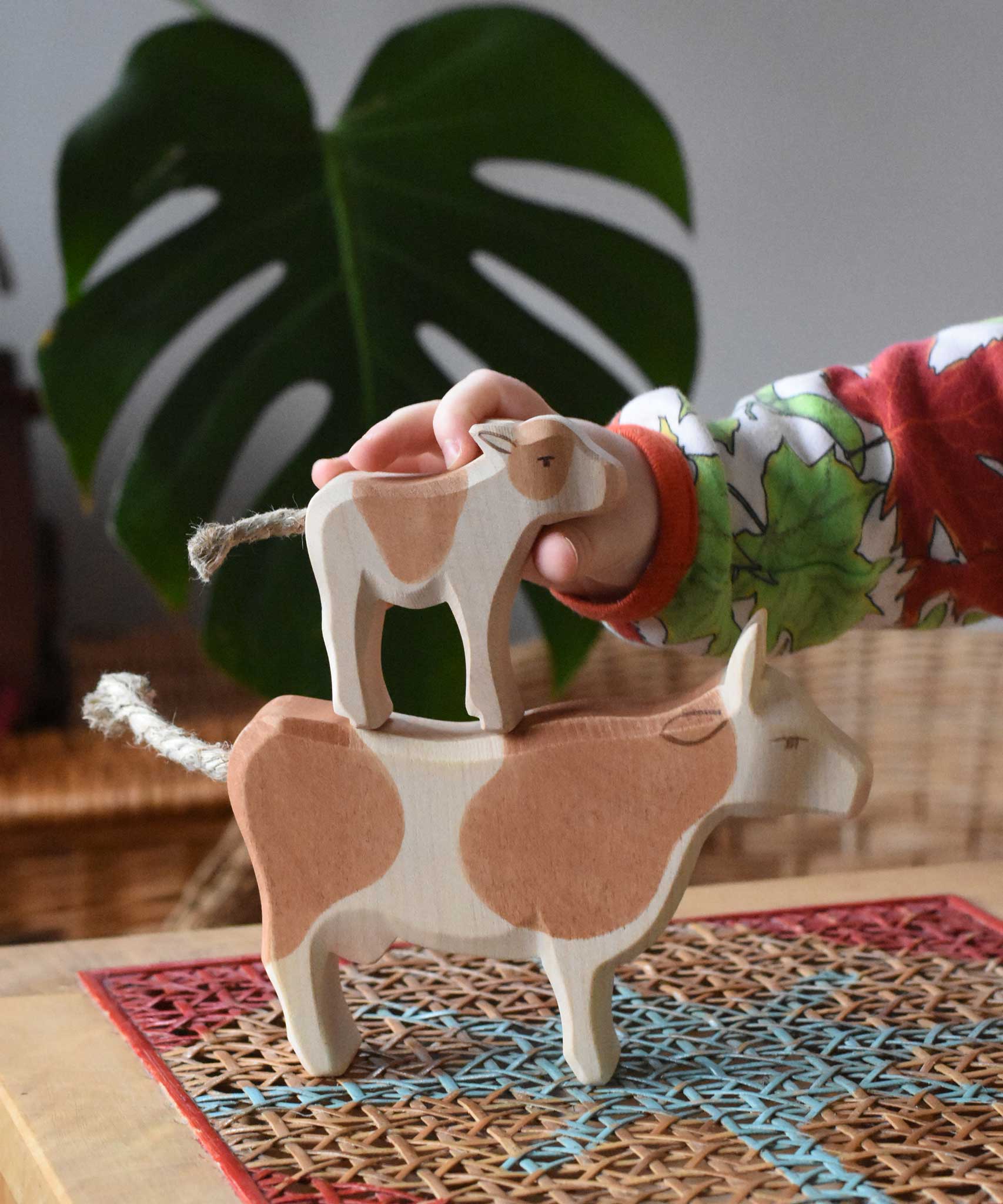 Child stacking a standing brown calf wooden toy figure on top of a brown cow figure.