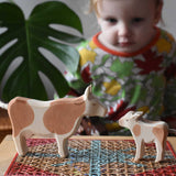 Child playing with Ostheimer wooden toy brown cow and calf figures.