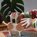 Child stacking a standing brown calf wooden toy figure on top of a brown cow figure.