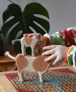Child stacking a standing brown calf wooden toy figure on top of a brown cow figure.