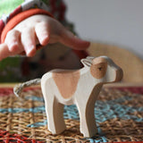 Child's hand reaching for an Ostheimer brown standing calf wooden toy figure. 
