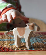 Child's hand reaching for an Ostheimer brown standing calf wooden toy figure. 