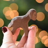 An Ostheimer Brown standing lamb wooden toy figure placed on a wooden surface. This wooden figure is part of a large range of expertly hand crafted, Waldorf inspired, wooden toys here at Babipur. 