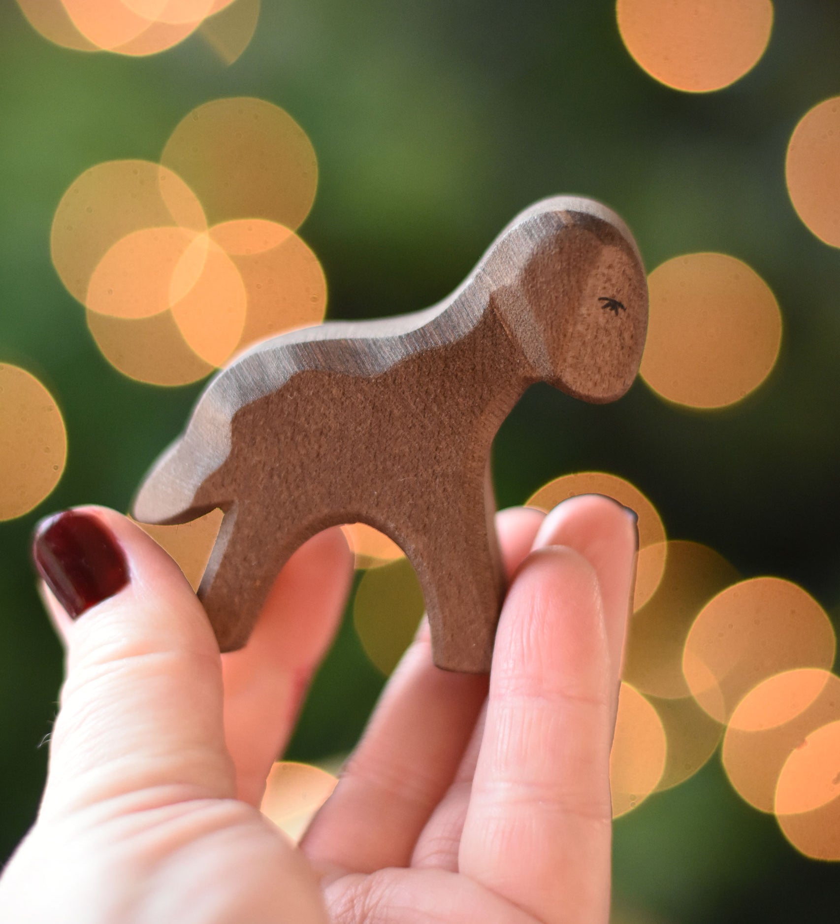 An Ostheimer Brown standing lamb wooden toy figure placed on a wooden surface. This wooden figure is part of a large range of expertly hand crafted, Waldorf inspired, wooden toys here at Babipur. 
