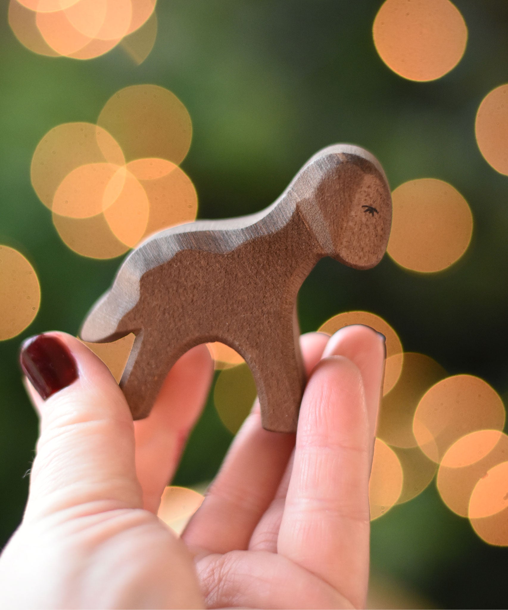 An Ostheimer Brown standing lamb wooden toy figure placed on a wooden surface. This wooden figure is part of a large range of expertly hand crafted, Waldorf inspired, wooden toys here at Babipur. 