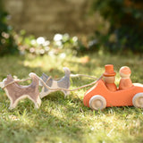 Ostheimer standing and running sled dogs tied by string to an orange Grimm's car with two Grapat peg dolls placed inside in the Babipur garden.