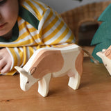 Ostheimer brown and white cow wooden toy figure placed on a wooden surface with a child in the background looking on.