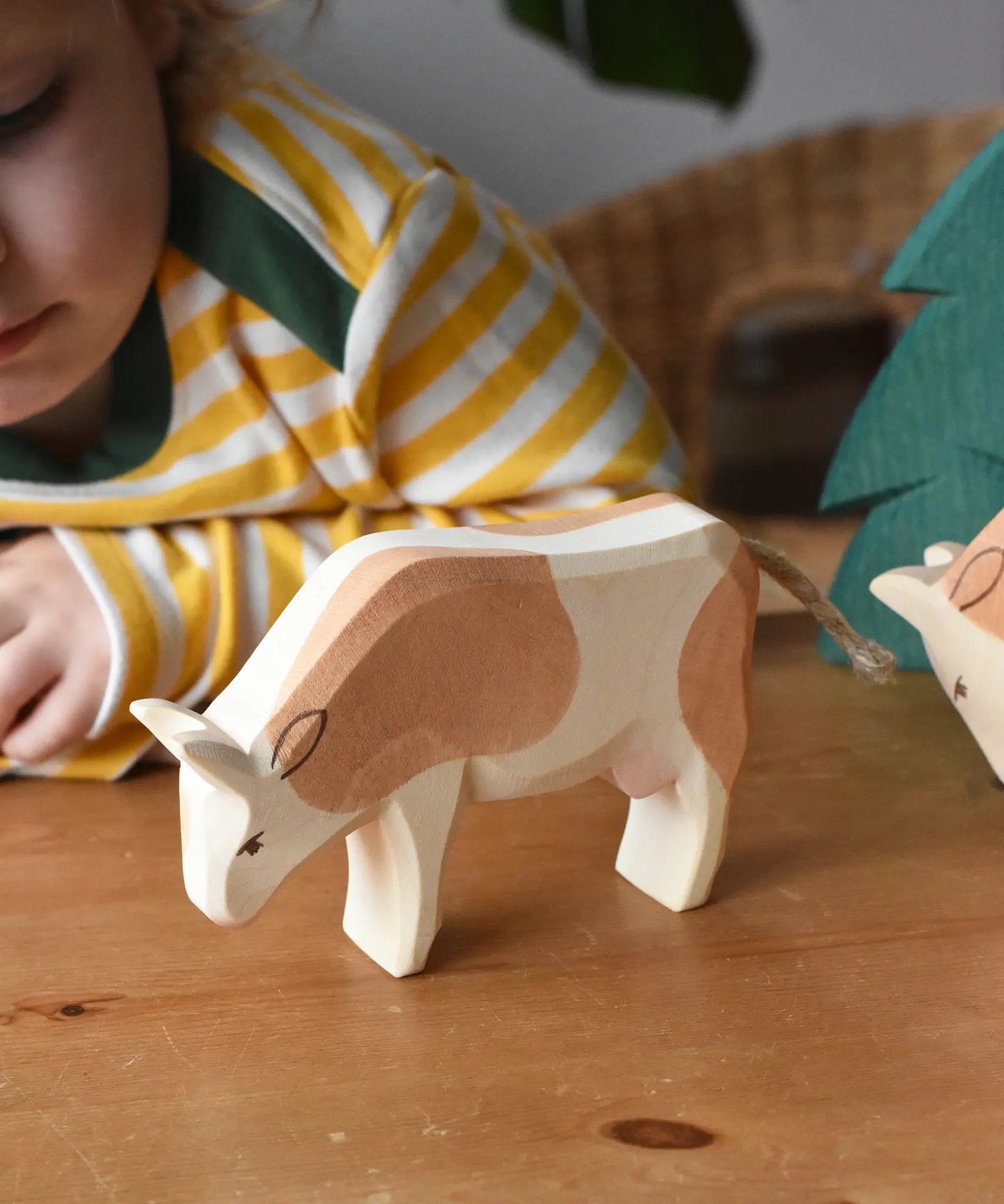 Ostheimer brown and white cow wooden toy figure placed on a wooden surface with a child in the background looking on.