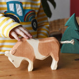 Child's hand petting the Ostheimer brown and white ox wooden toy figure. 