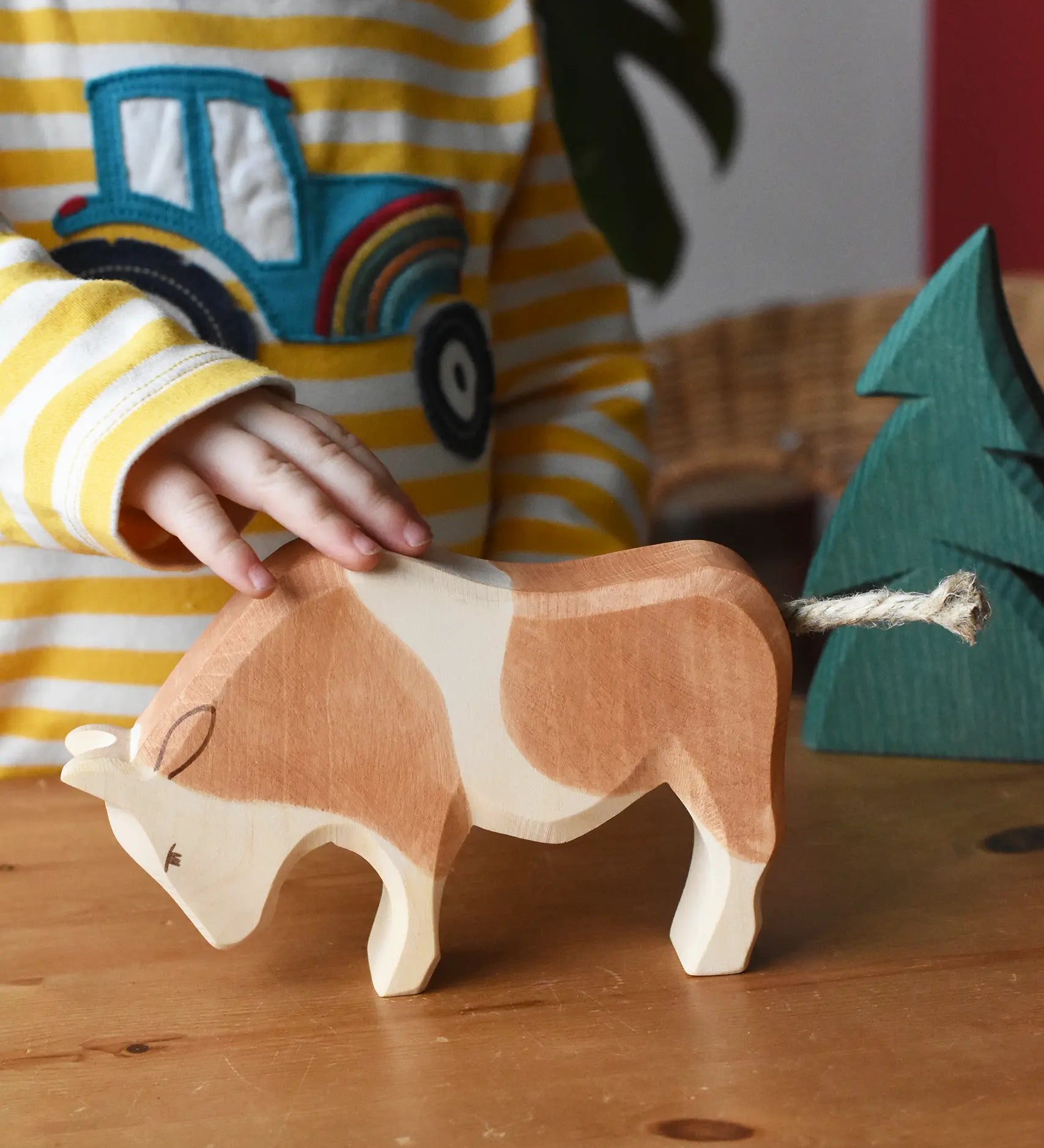 Child's hand petting the Ostheimer brown and white ox wooden toy figure. 