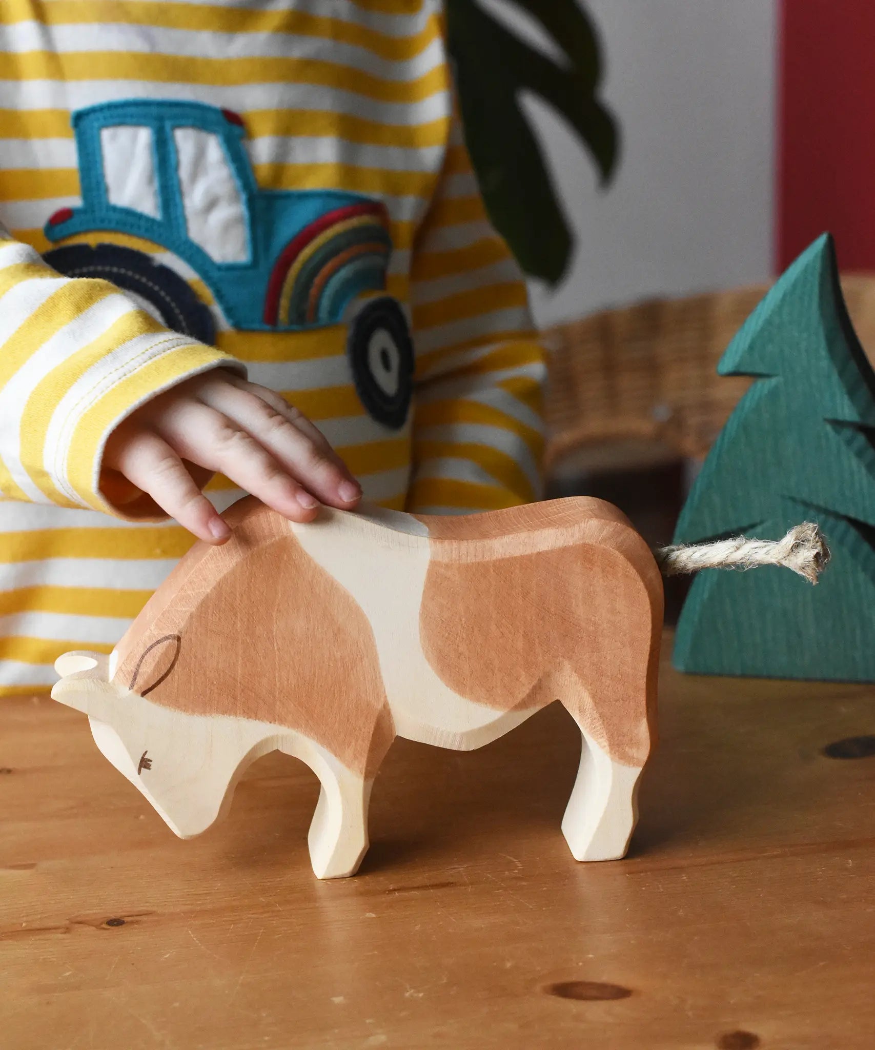 Child's hand petting the Ostheimer brown and white ox wooden toy figure. 