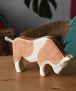 Ostheimer brown and white ox wooden toy figure placed on a wooden surface.
