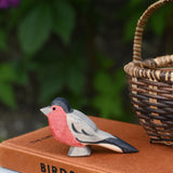 An Ostheimer bullfinch wooden toy bird figure placed on top a pile of old books next to a Kraul basket.