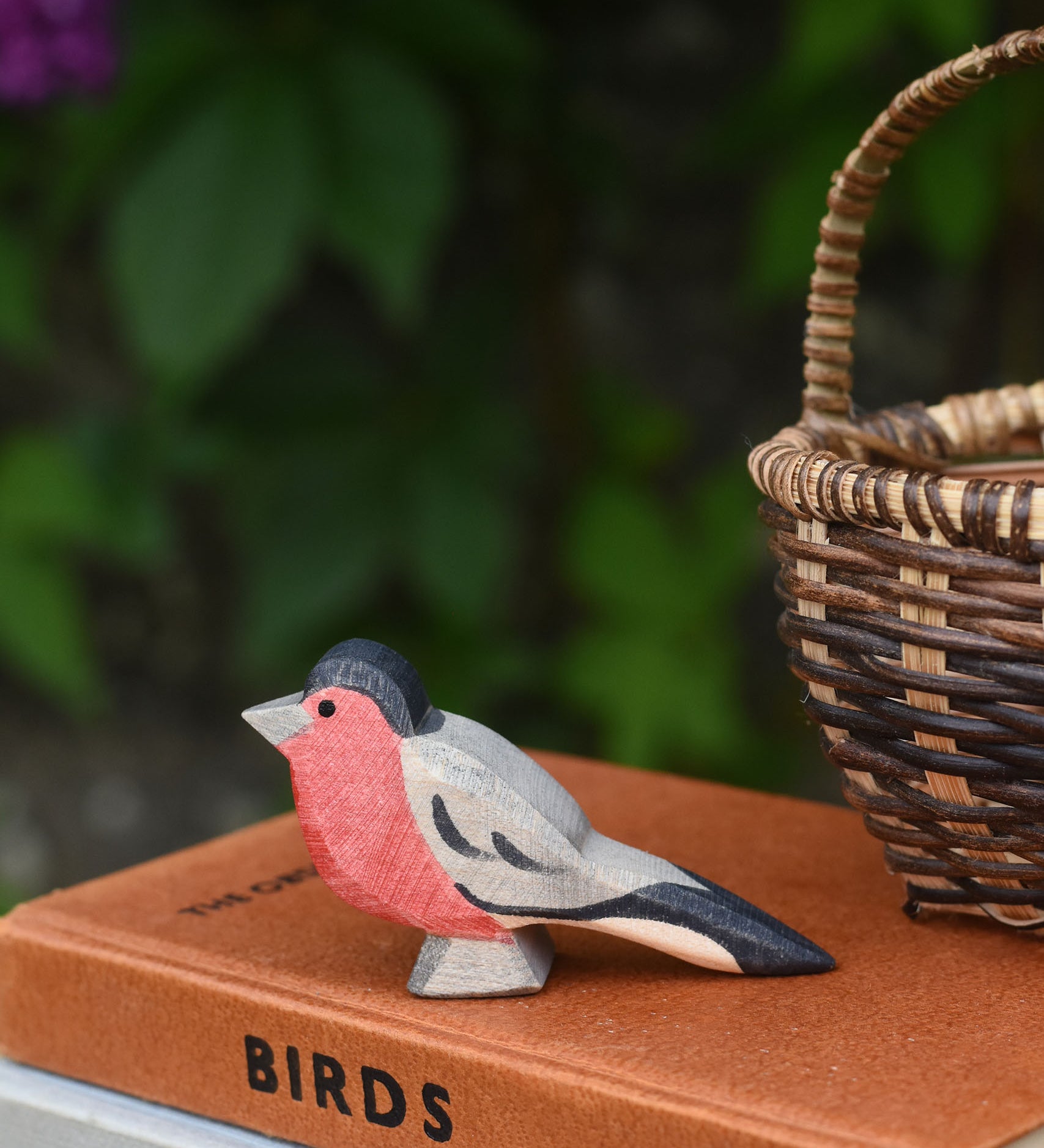 An Ostheimer bullfinch wooden toy bird figure placed on top a pile of old books next to a Kraul basket.