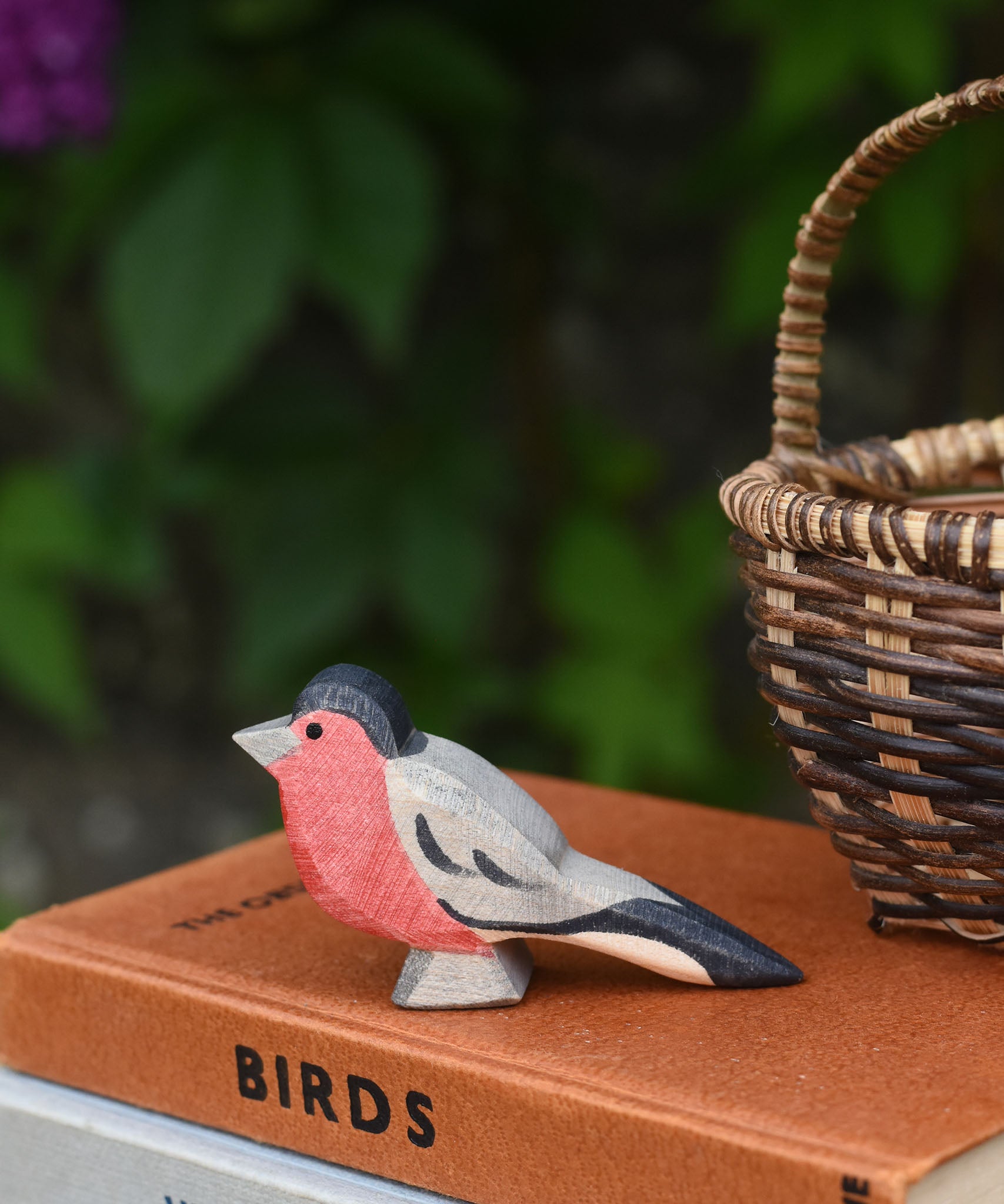 An Ostheimer bullfinch wooden toy bird figure placed on top a pile of old books next to a Kraul basket.