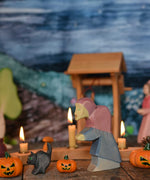 Ostheimer hand made and hand painted wooden witch and cat figures  placed on a wooden surface in a seasonal display. An Ostheimer wooden well can be seen in the background along with other wooden figures and a Grimm's celebration ring. These wooden figures are part of a wide range of expertly hand crafted wooden toys here at Babipur. 